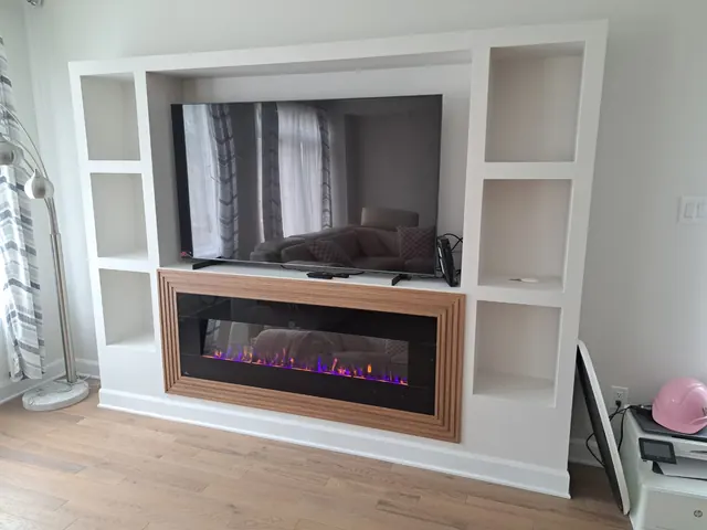 White built-in media wall with open shelves, a TV and an electric fireplace in a wood surround